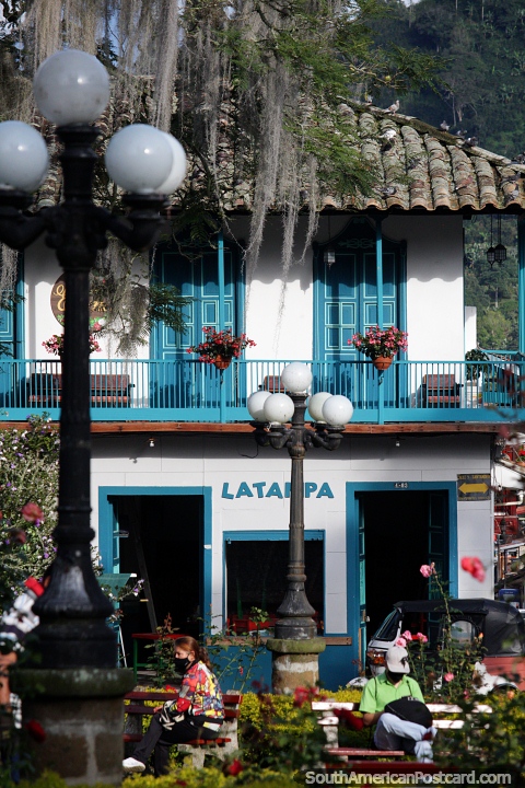 Atractivo edificio con balcón y puertas de color azul brillante, ubicado en el parque de Jardin. (480x720px). Colombia, Sudamerica.