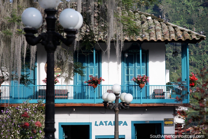 Hermoso edificio debajo de un techo de tejas, flores se sientan a lo largo del balcón de madera en Jardin. (720x480px). Colombia, Sudamerica.