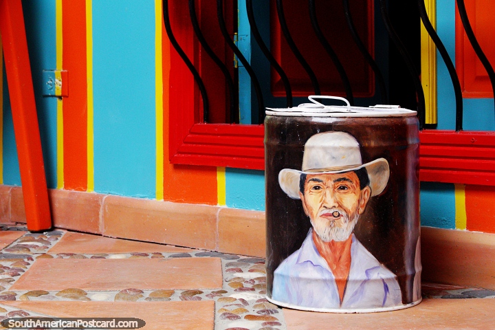 Man with a hat painted on a canister , a colorful and bright wall, a patio in Jardin. (720x480px). Colombia, South America.