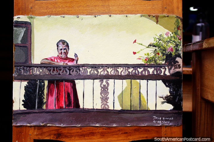 Woman stands on her balcony with flowers, a painted chair by Jose Daniel in Jardin. (720x480px). Colombia, South America.