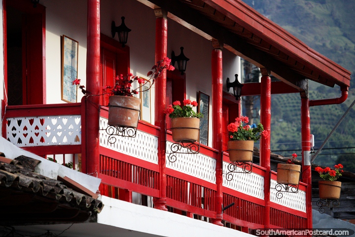 Casa roja brillante con flores del mismo color, luz del sol en el balcón en Jardin. (720x480px). Colombia, Sudamerica.