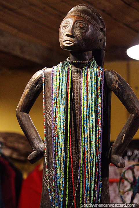 Carved from wood, an indigenous figure wearing colored beads, art in Salento. (480x720px). Colombia, South America.