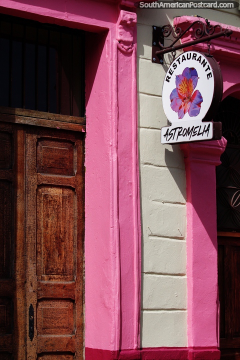 Fachada rosa y puerta de madera de un restaurante en La Candelaria en Bogotá, calles coloridas. (480x720px). Colombia, Sudamerica.