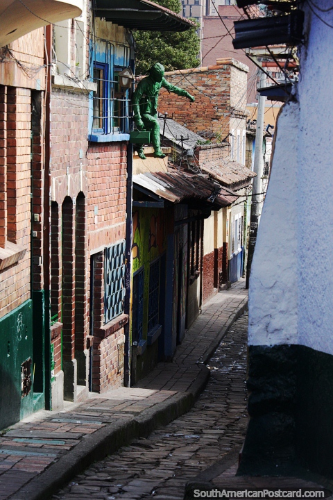 Homem verde olha para uma rua estreita de paraleleppedos em La Candelaria, em Bogot. (480x720px). Colmbia, Amrica do Sul.