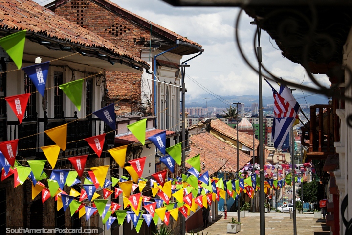 Bandeiras coloridas descem pela rua, casas de tijolos vermelhos e telhados vermelhos, Bogot  cativante. (720x480px). Colmbia, Amrica do Sul.