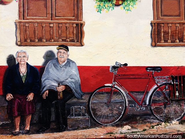 O homem e a mulher mais velhos esto sentados do lado de fora de uma casa, uma bicicleta ao lado, um mural na lateral de uma casa em Sogamoso. (640x480px). Colmbia, Amrica do Sul.