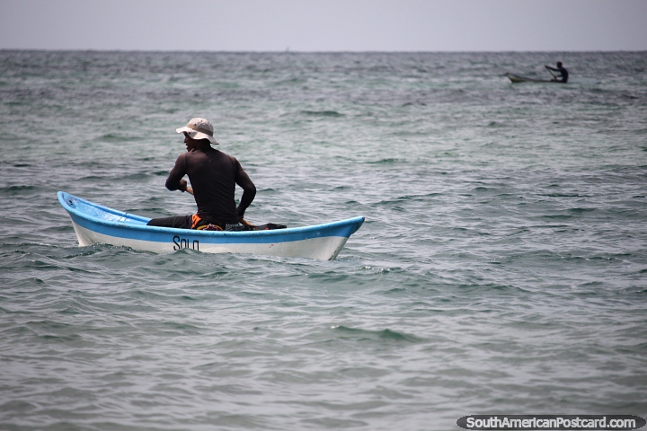 One man solo in a canoe at sea but he has a distant companion, locals of Tintipan Island. (720x480px). Colombia, South America.