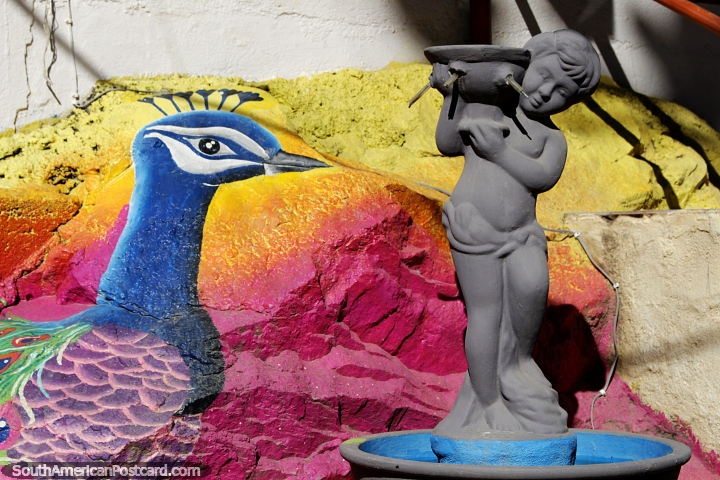 Fonte com um mural colorido pintado atrás de um grande pavão em Minca. (720x480px). Colômbia, América do Sul.
