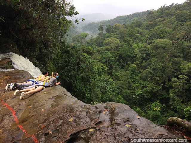 2 people look over the cliff at the End of the World Waterfall while attached to chains in Mocoa. (640x480px). Colombia, South America.