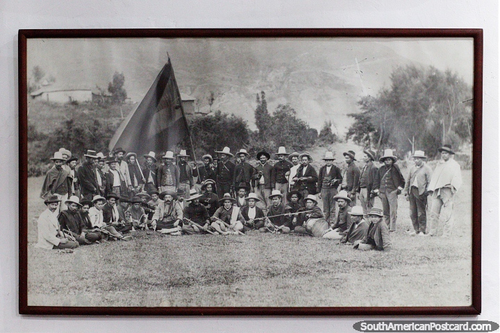 Old black and white photograph of locals of Pamplona, many men in hats with large flag. (720x480px). Colombia, South America.