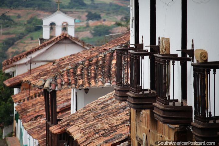 Varandas de madeira em uma fileira, telhados vermelhos e uma torre de igreja distante em Barichara. (720x480px). Colmbia, Amrica do Sul.