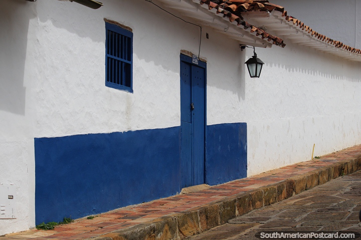 Paredes caiadas de branco de uma casa em Barichara, uma porta e janela azuis e uma lanterna. (720x480px). Colômbia, América do Sul.