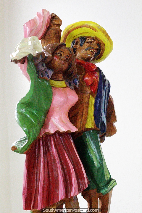 Homem e mulher vestidos com uma grande variedade de cores danam, esculturas em madeira no museu do carnaval, Pasto. (480x720px). Colmbia, Amrica do Sul.