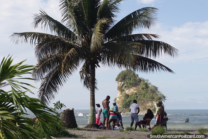 Morro beach with the small island in the bay and people under a palm tree. (720x480px). Colombia, South America.