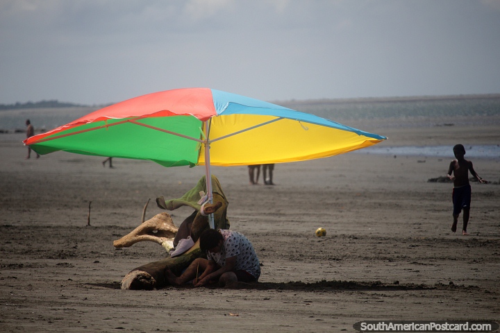 Colorful umbrella really stands out with a background of sand far into the distance in Tumaco. (720x480px). Colombia, South America.