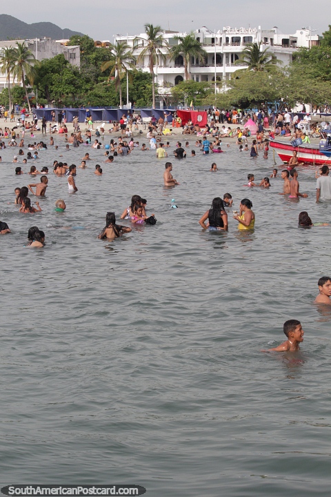 People enjoy cooling off at the beach on a hot day in Santa Marta. (480x720px). Colombia, South America.