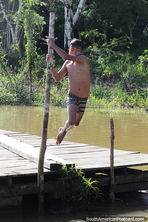 Menino local da comunidade Mocagua Amazona pula na gua usando um poste de madeira perto de Leticia. (480x720px). Colmbia, Amrica do Sul.