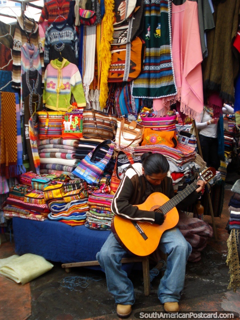 Bright colored bags and clothing with guitar playing salesman in Otavalo. (480x640px). Ecuador, South America.