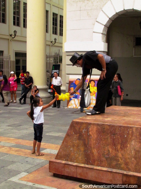 A menina recebe um animal de balão de um palhaço em Praça da Administracion, Guayaquil. (480x640px). Equador, América do Sul.