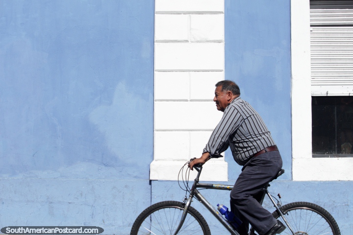Man on a bicycle rides past a blue and white wall in Riobamba. (720x480px). Ecuador, South America.