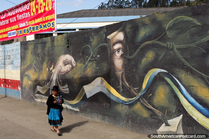 Quechua woman with a black hat and blue dress walks past a mural in Biblian. (720x480px). Ecuador, South America.