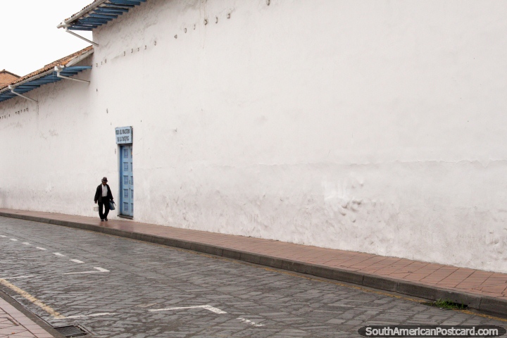 O homem anda para além de uma porta azul ao longo de uma parede branca longa em Cuenca. (720x480px). Equador, América do Sul.