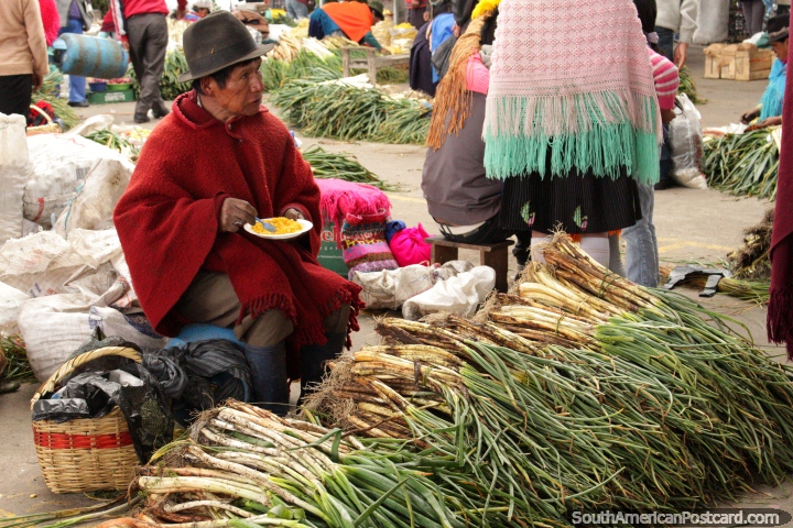 O homem em chapéu e xale come o arroz e vende cebolas de primavera em Praça Kennedy, Saquisili. (720x480px). Equador, América do Sul.