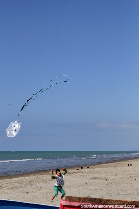 O rapaz voa um pequeno papagaio de papel em um grande céu na praia em El Matal. (480x720px). Equador, América do Sul.