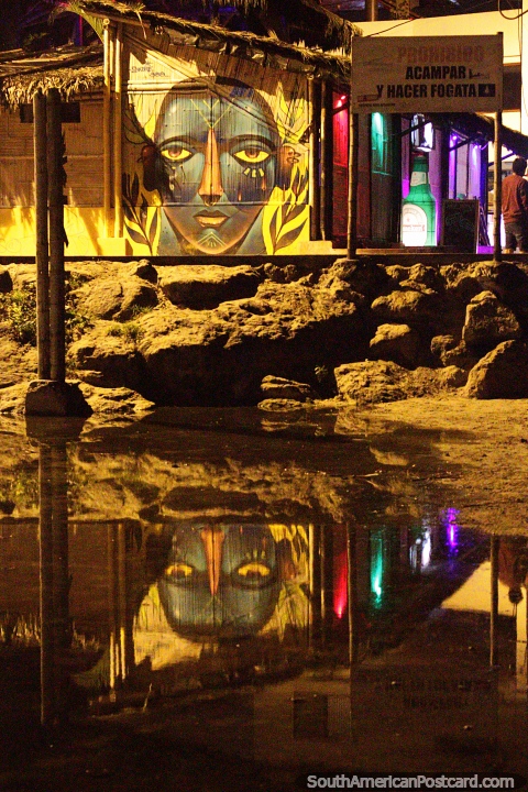 Cara grande, arte callejero con reflejo junto a un bar y la playa en Montañita. (480x720px). Ecuador, Sudamerica.