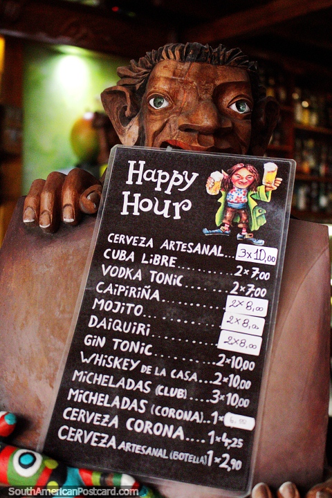 Happy hour menu held by an elf wooden carving, nice decor in Banos. (480x720px). Ecuador, South America.