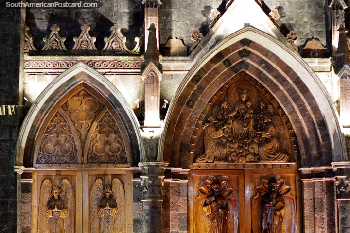Large arched wooden doors with intricate engraved sculptures, facade of the church in Banos at night. (720x480px). Ecuador, South America.