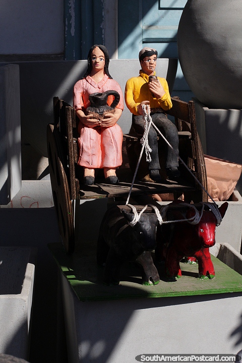 Hombre y mujer sentados en un carro tirado por vacas, arte hecho en Aregua. (480x720px). Paraguay, Sudamerica.