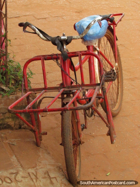 A bicicleta vermelha instalou-se na rua de pedra arredondada vermelha em Concepcion. (480x640px). Paraguai, Amrica do Sul.