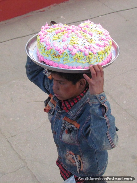 O rapaz transporta o bolo delicioso com a camada de açúcar rosa/amarela sobre o seu chefe, Huamachuco. (480x640px). Peru, América do Sul.