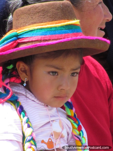 Young girl with brown hat and colorful bands watches street dancing in Huaraz. (480x640px). Peru, South America.