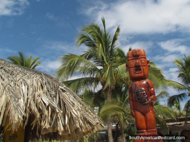 Carved wooden figure in front of palm trees and a cabana in Mancora. (640x480px). Peru, South America.