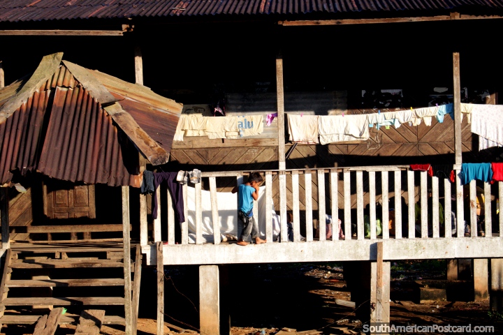 El niño joven sube a lo largo del balcón de su casa de madera en el Amazonas entre Pucallpa y Aguaytia. (720x480px). Perú, Sudamerica.