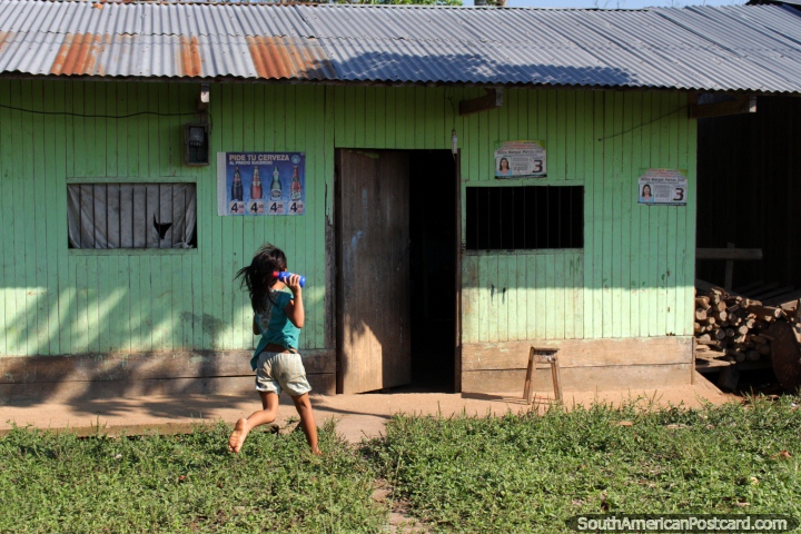 A menina corre para casa com uma garrafa de algo, casa simples no Amaznia em volta de Aguaytia. (720x480px). Peru, Amrica do Sul.