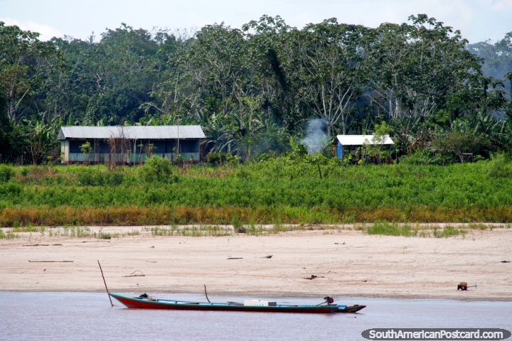 Motorized river canoe and distant Amazon houses, south of Lagunas. (720x480px). Peru, South America.