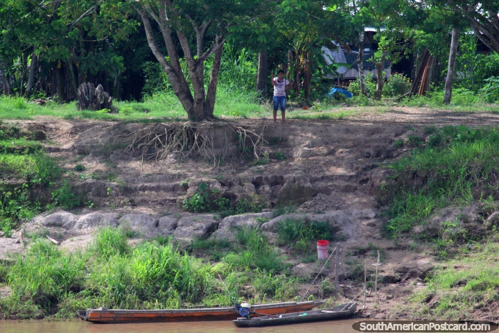 Una mujer observa el ferry pasar de su propiedad en la orilla del ro en la Amazonas. (720x480px). Per, Sudamerica.