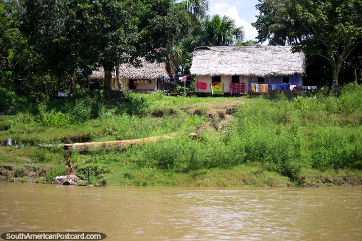 Boy on the left plays beside the river, his house behind, Amazon living, west of Santa Rosa. (720x480px). Peru, South America.