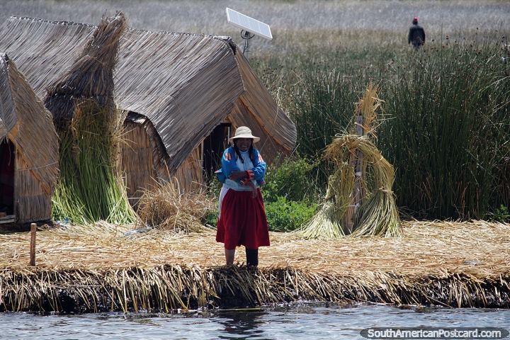 La gente de los Uros vive en islas de juncos flotantes en el lago Titicaca, una mujer afuera de casas con techo de paja, Puno. (720x480px). Per, Sudamerica.