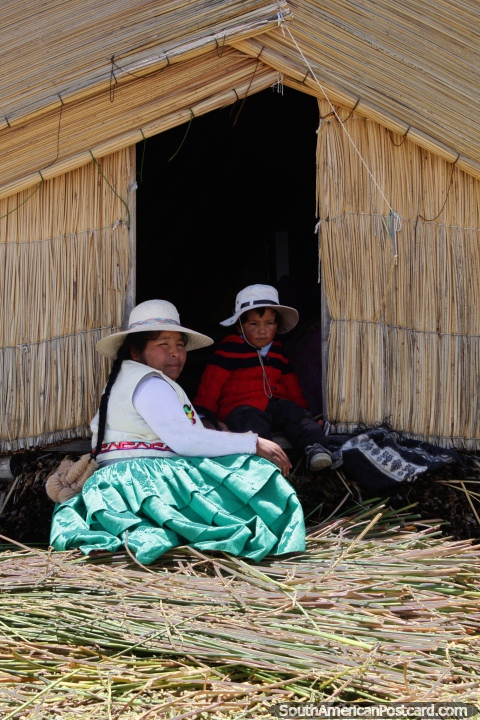 Uma mãe Uros e seu filho do lado de fora da sua casa coberta com palha em Lago Titicaca em Puno. (480x720px). Peru, América do Sul.