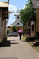 Woman with purple umbrella walks in front of the church in Saint Georges, French Guiana.