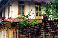 Flores de color rosa, una pared de ladrillo oscuro y un antiguo edificio en Cayenne, Guayana Francesa. Las 3 Guayanas, Sudamerica.