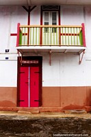 A pink and green balcony and a pink door below in Cayenne, French Guiana.