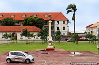 Old and new buildings with tiled roofs and a monument, the sea behind, Cayenne, French Guiana.