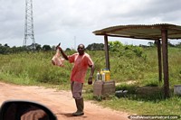 Homem que vende pernas de carne da margem de estrada perto de Saint Laurent du Maroni em Guiana Francesa. As 3 Guianas, América do Sul.