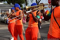 Versão maior do Os trombeteiros vestiram-se na cor-de-laranja com agasalhos dianteiros azuis na pompa de Avondvierdaagse em Paramaribo, Suriname.