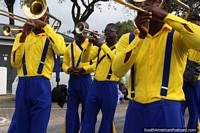 Versión más grande de The New Experience Brassband soplar trompetas, vestida de amarillo y azul, el desfile Avondvierdaagse en Paramaribo, Surinam.